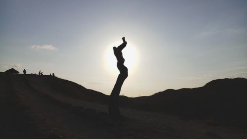 Silhouette woman with arms raised standing against sky during sunset