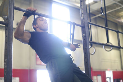 Confident male adaptive athlete screaming while doing chin-ups in gym