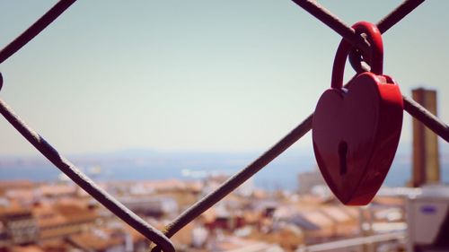 Close-up of heart shape padlock on chainlink fence against sky during sunny day