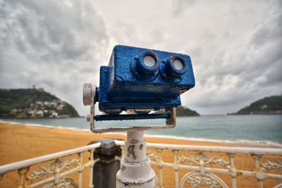 Close-up of coin-operated binoculars by sea against sky