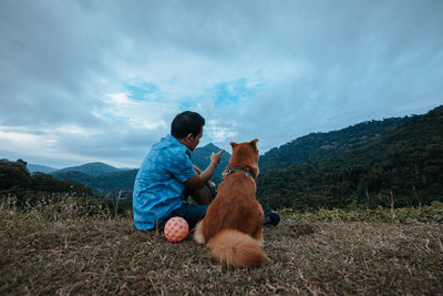 Rear view of dog sitting on land against sky