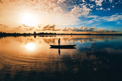 Silhouette man on boat in lake against sky during sunset