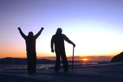 Silhouette friends standing on snowcapped mountains at sunset