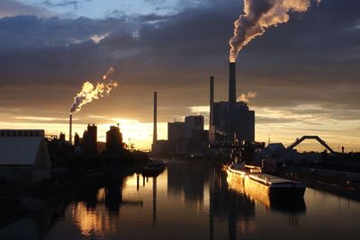 Factories emitting smoke against cloudy sky during sunset