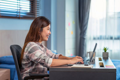 Side view of young woman using phone while sitting on table