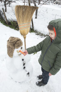 Full length of smiling boy standing by snowman in yard during winter