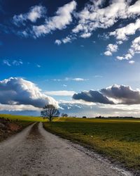 Road by agricultural field against sky