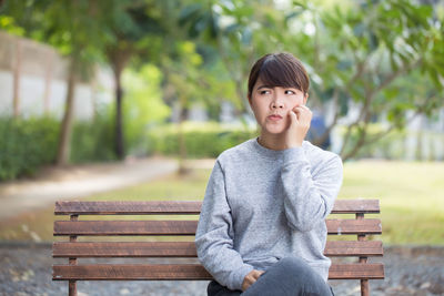 Young woman scratching cheek while sitting on bench at park