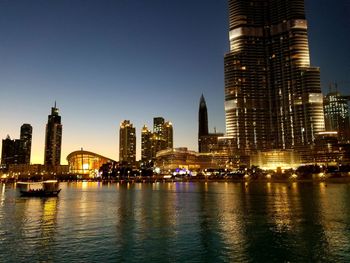 Illuminated buildings by river against sky in city