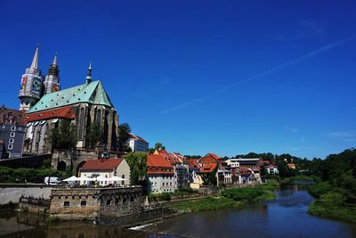 Town by river and buildings against blue sky