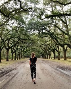 Rear view of woman walking on road amidst trees