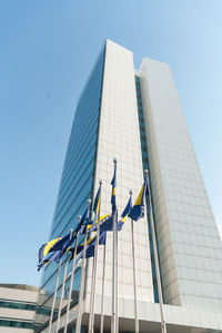 Low angle view of bosnia and herzegovinan flags and modern building against clear blue sky