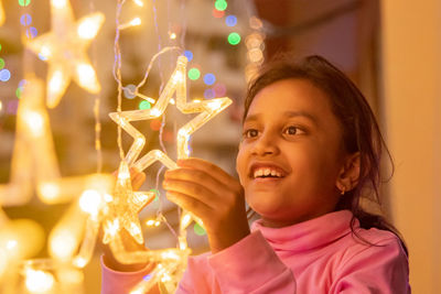 Close-up of young woman holding illuminated string lights at home