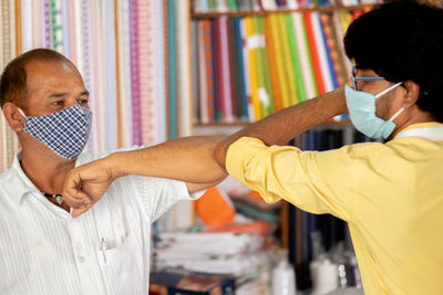 Men wearing flu mask touching elbow at store