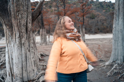 Happy woman standing by tree trunk in forest