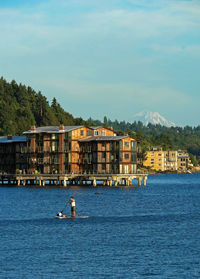 Man paddleboarding on lake with buildings in background