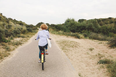 Rear view of friends riding bicycles on road against sky