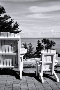 Chairs and table by sea against sky