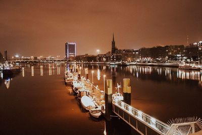 Boats moored in river by illuminated buildings against sky at night