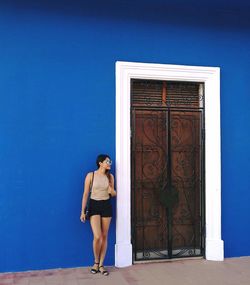 Full length of young woman standing against blue building