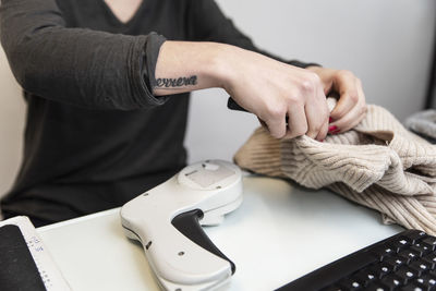 Midsection of woman scanning clothes while sitting at table in store