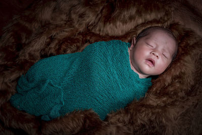 High angle view of cute sleeping baby girl wrapped in textile lying on fur