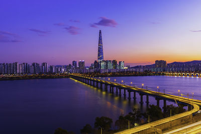 Illuminated buildings by river against sky at night