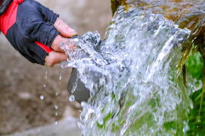 The flow of pure spring water. man's hand collects water in mug in crystal cool spring.