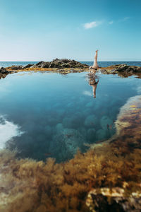 Woman standing on rock by sea against sky