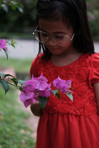 Girl wearing oversized eyeglasses while looking at pink flowering plants in park