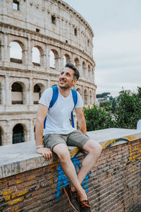 Portrait of young man sitting against old building, tourist roma italy colosseum rome italia 