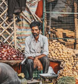Mature man selling vegetables while sitting at market