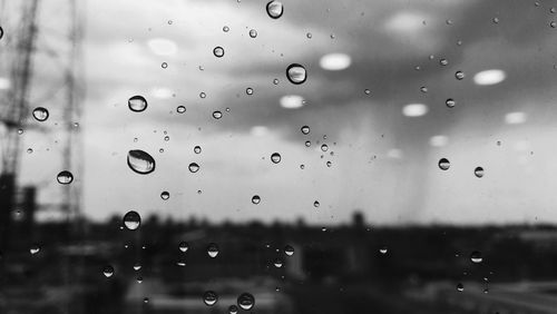 Close-up of water drops on window against sky