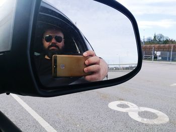 Reflection of man photographing on side-view mirror