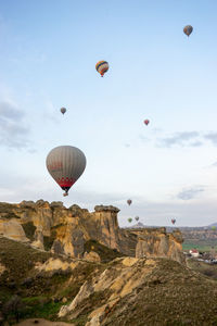 Hot air balloons flying over rock formation against sky