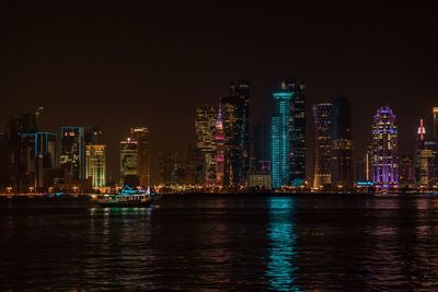 Illuminated buildings by sea against sky at night