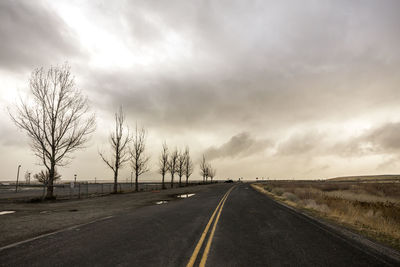 Road amidst bare trees against sky