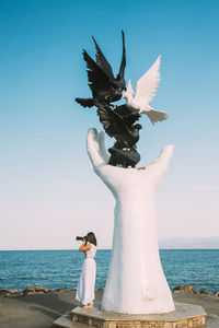 Rear view of woman standing by sea against sky during sunset