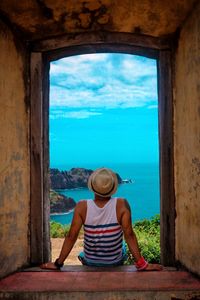 Rear view of man sitting on doorway while looking at sea