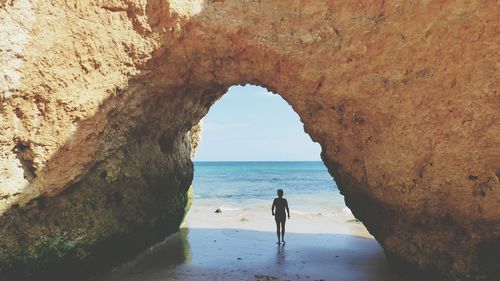 Boy standing under rock formation at beach