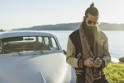 Young man checking his cell phone near a scenic lake