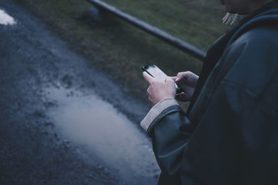 Cropped image of woman using smart phone on wet road