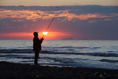 Man fishing on beach during sunset