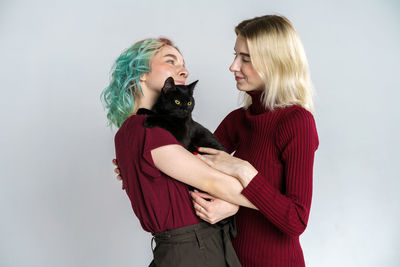 Portrait happy girls in casual clothes on light background, holding black cat