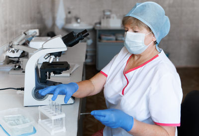 Woman scientist wearing protective gloves, hat and mask working in laboratory making a covid test