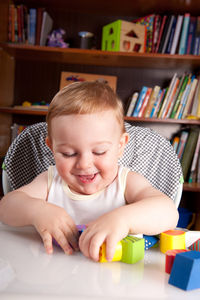 Cheerful cute baby boy playing with toy blocks on table