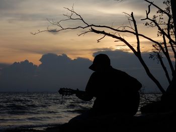 Rear view of silhouette man by sea against sky during sunset