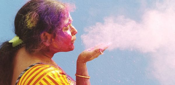 Young woman blowing powder paint while standing against wall