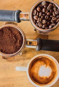 High angle view of coffee cup by beans and powder in portafilter on table