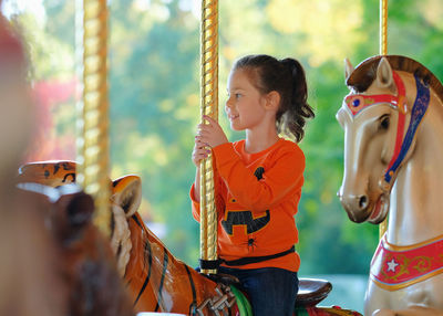 Pretty girl in a halloween themed shirt is riding a carousel at the carnival